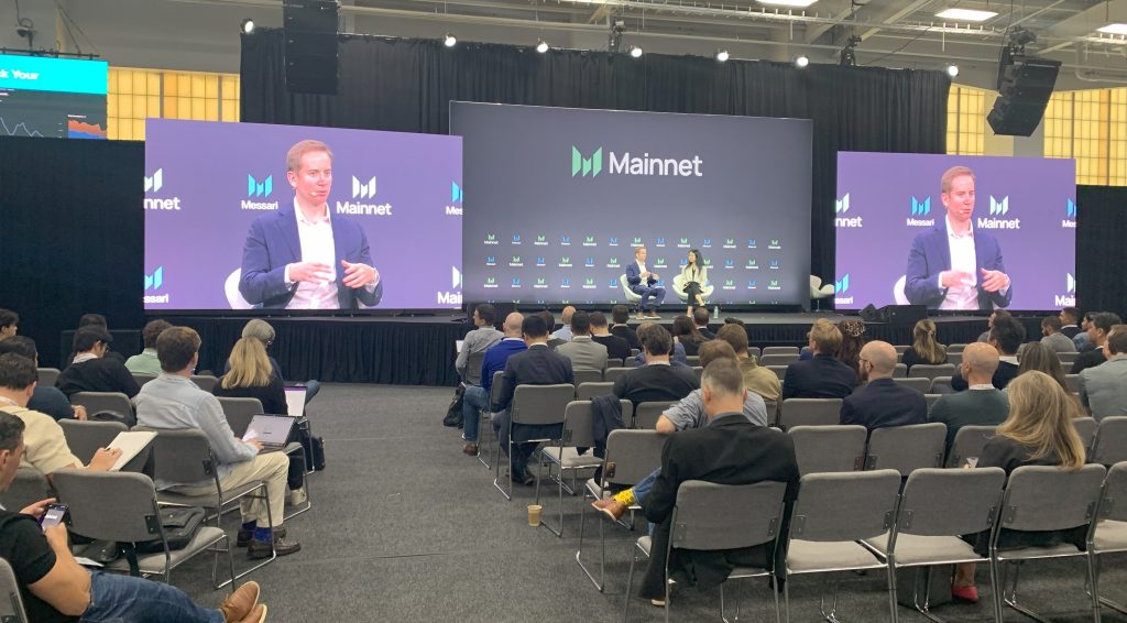 A shot of the larger Mainnet Macro stage and a talk in progress also showing attendees sitting in chairs listening.