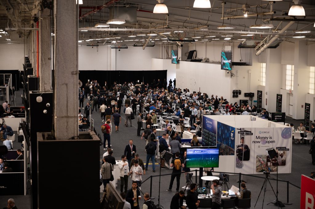 A shot from above of the inside of Pier 36 and a large crowd of conference attendees milling around at booths.